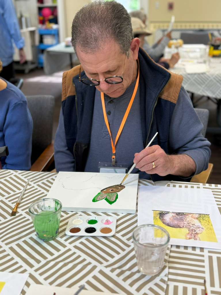 An Evergreen member painting at a table during an afternoon art session