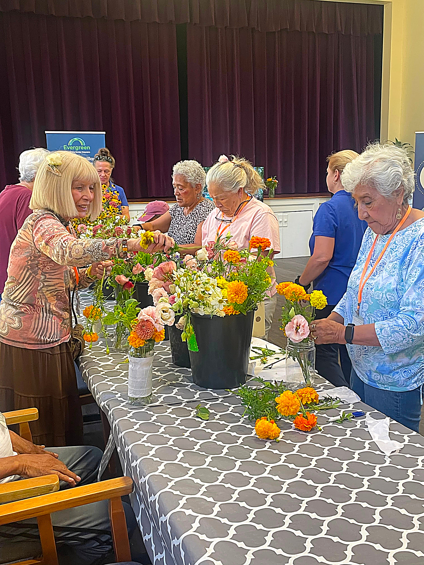 Evergreen members arranging fresh flowers together at a long table during a creative program
